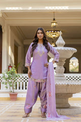Woman in a lavender traditional outfit standing in front of a decorative fountain.