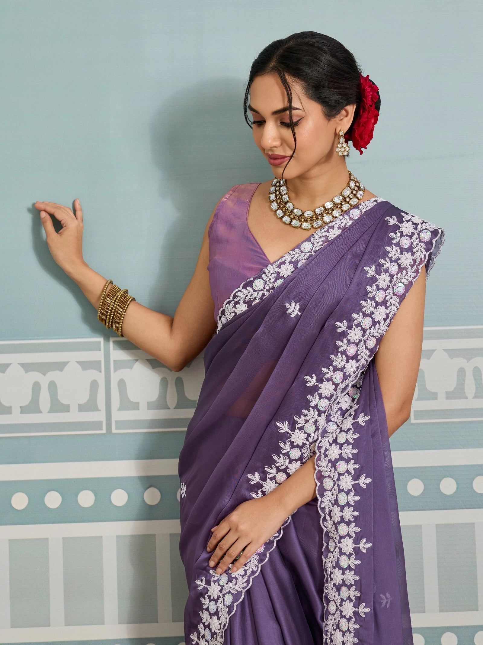 Woman wearing a purple saree with white embroidery against a light blue wall.