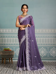 Woman wearing a purple saree with white embroidery against a decorative wall.