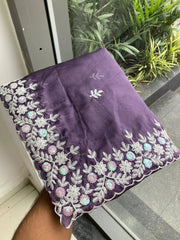 Purple fabric with floral embroidery held by a hand against a glass door with plants in the background