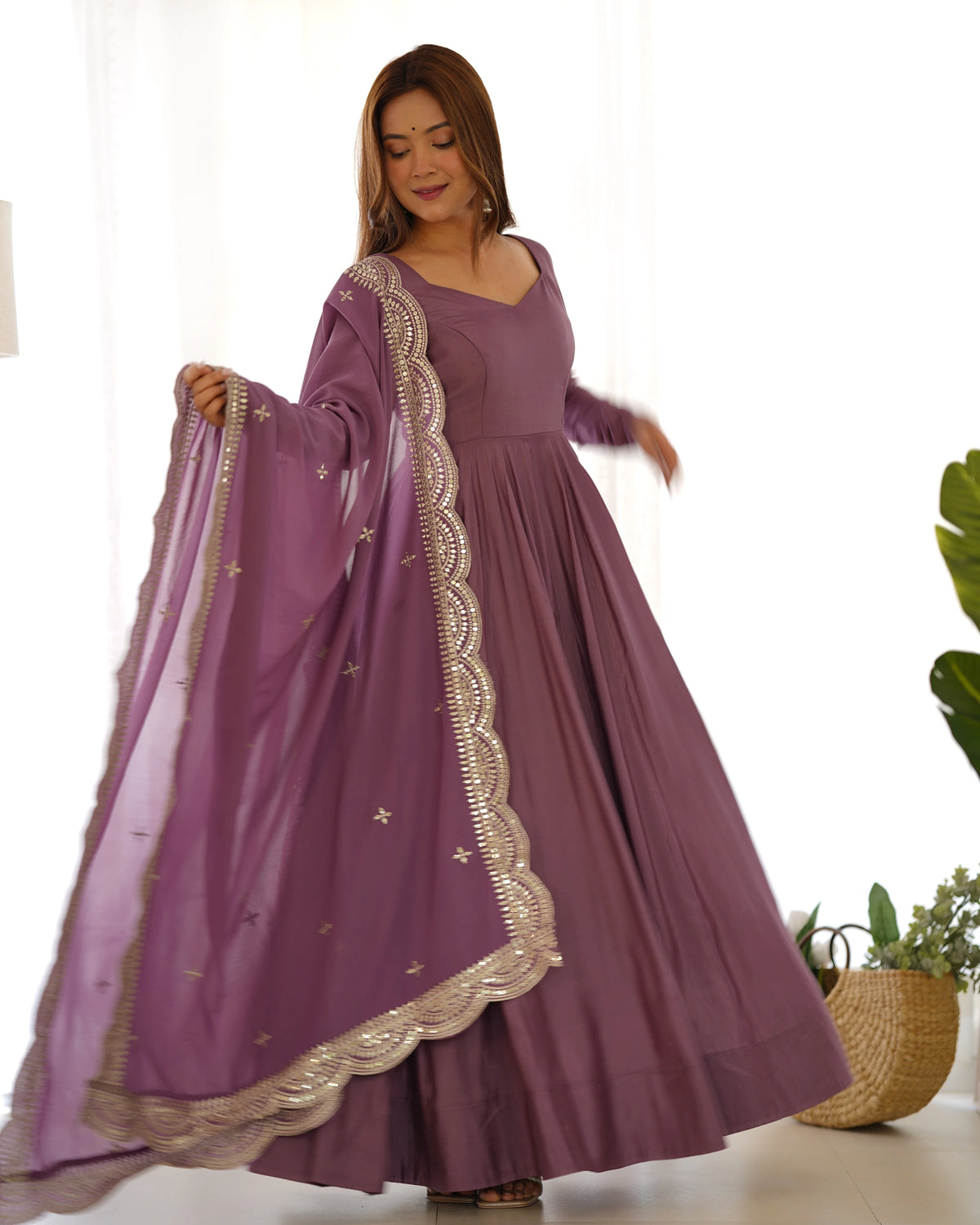 Woman wearing a purple dress with gold embroidery, holding a matching dupatta.