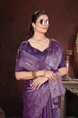 Woman wearing a purple saree with jewelry against a dark background