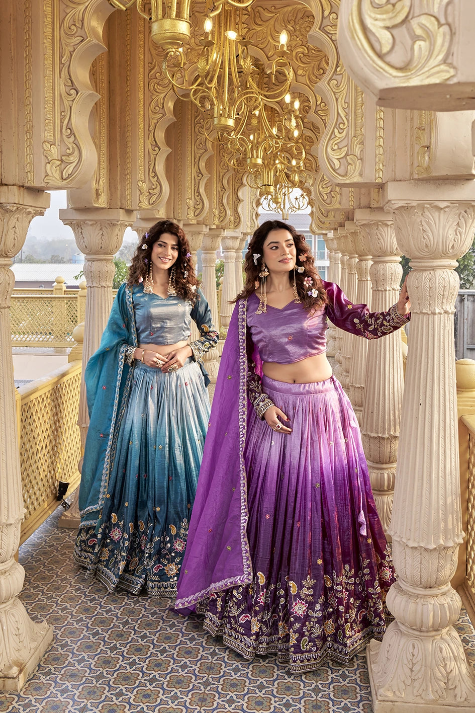 Two women in traditional outfits standing in an ornate indoor setting.
