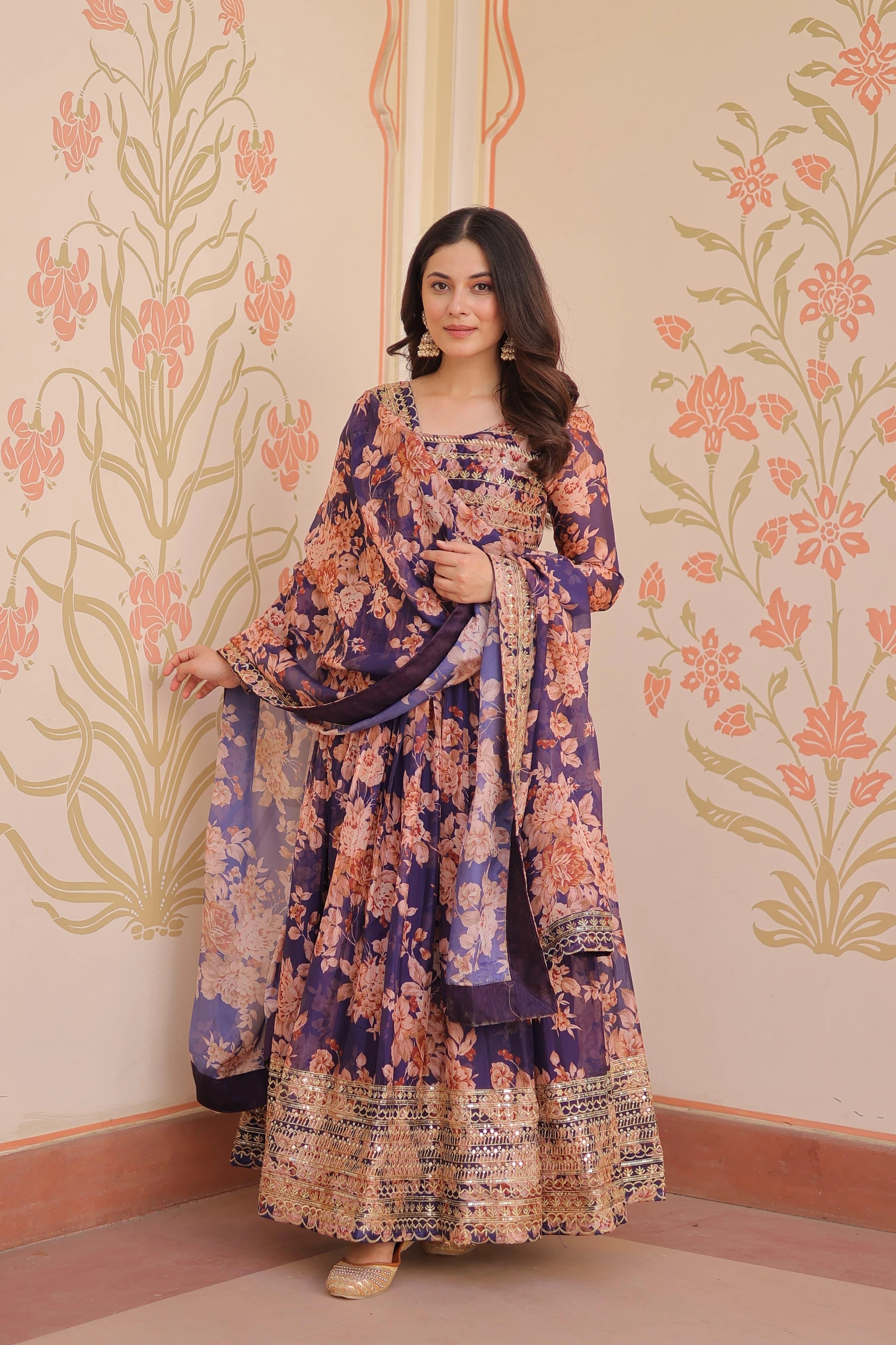 Woman in a floral dress standing against a decorative wall with floral patterns.