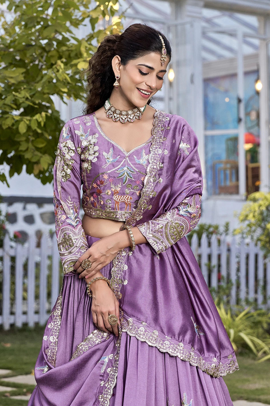 Woman in a purple traditional outfit with floral patterns standing outdoors.
