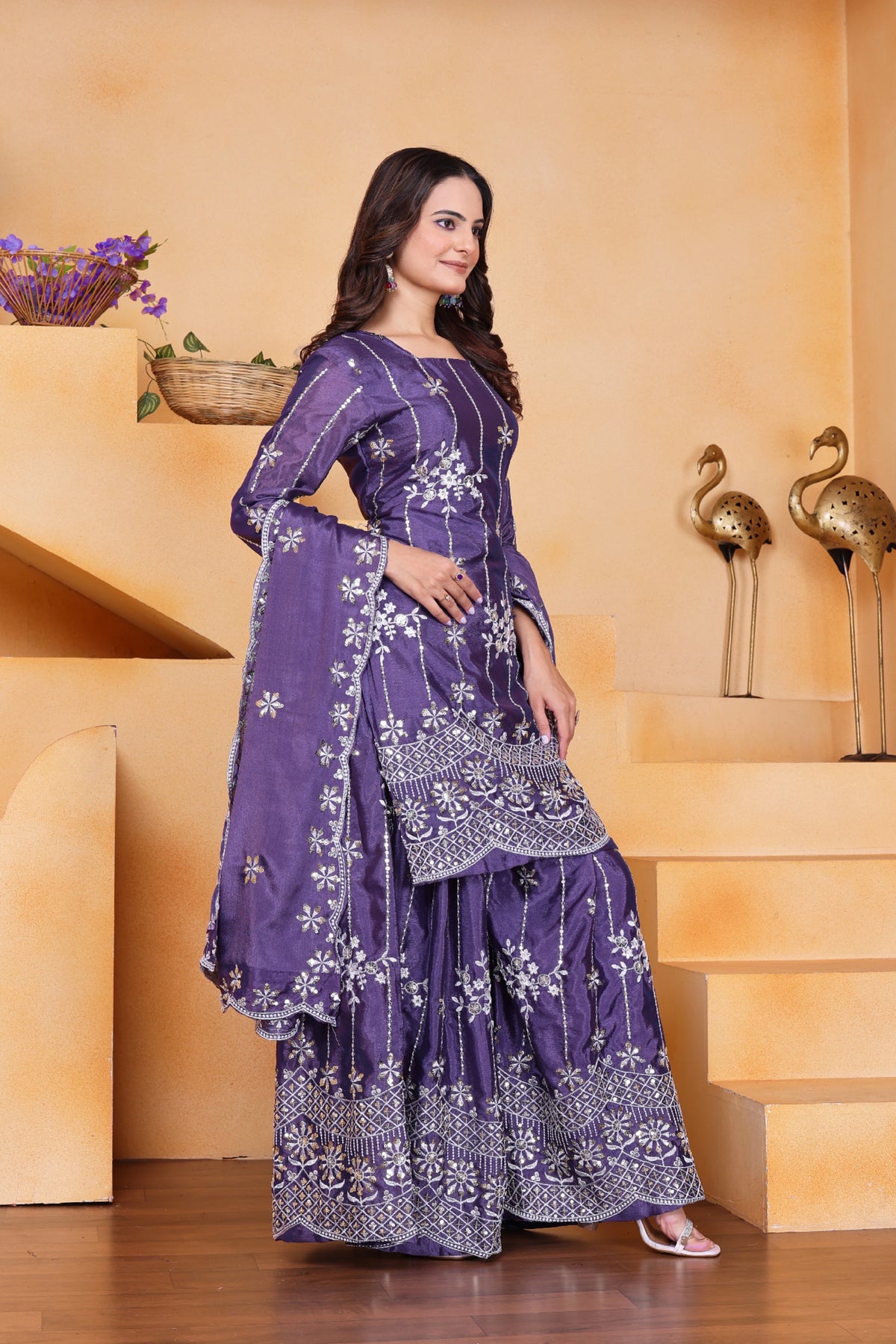 Woman in a purple traditional outfit standing in a decorative indoor setting.