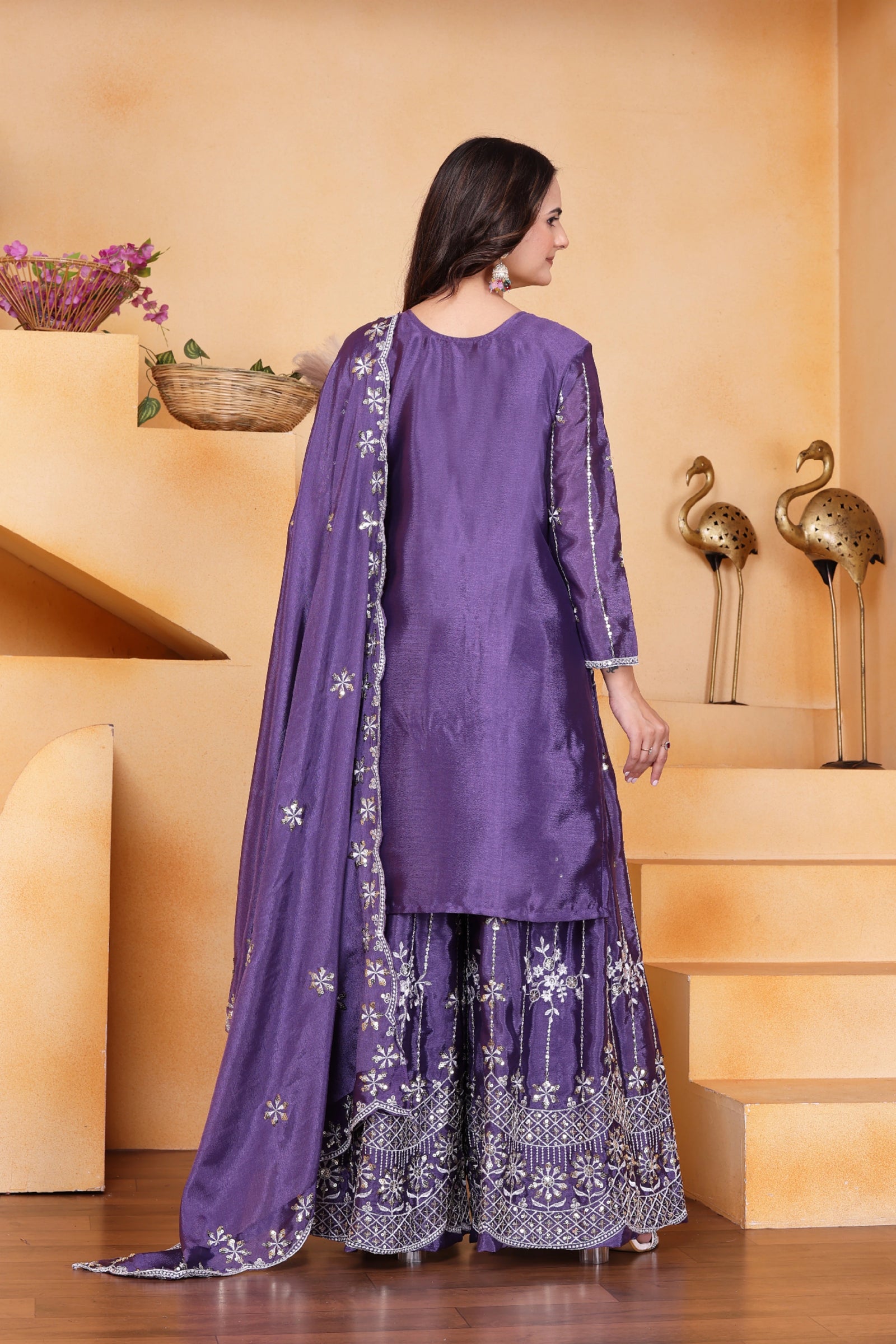Woman wearing a purple traditional outfit with white embroidery in a decorative setting.