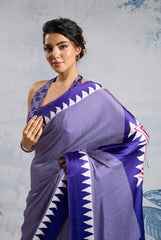 Woman wearing a purple saree with white patterns against a light gray background