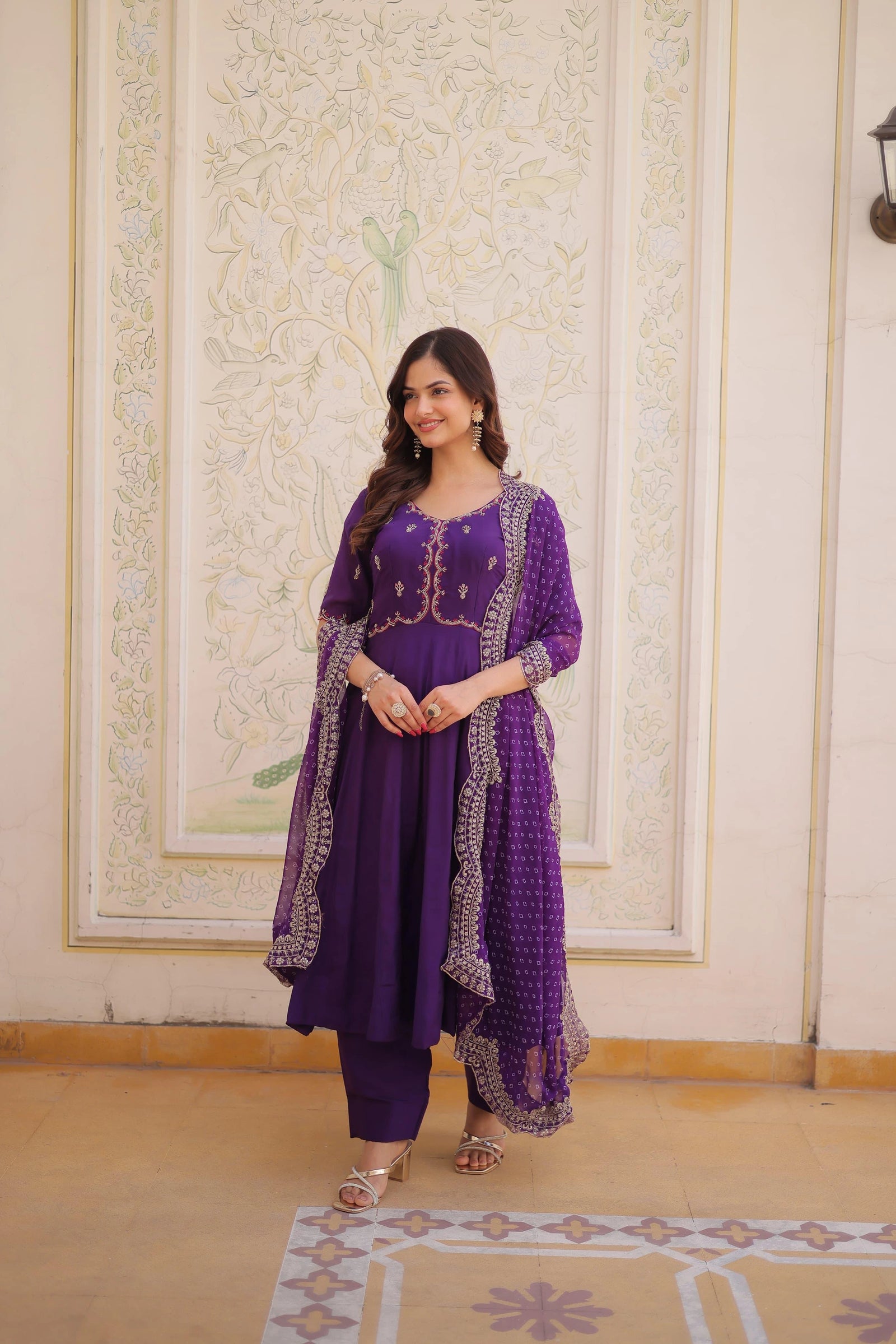 Woman wearing a purple traditional outfit with intricate designs in a decorated room.