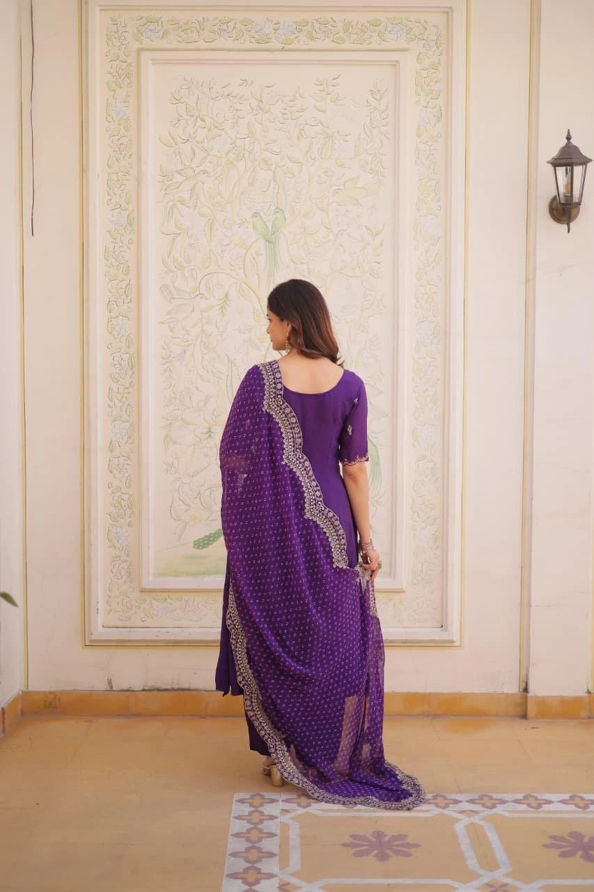 Woman in a purple saree standing in a room with decorative wall art.