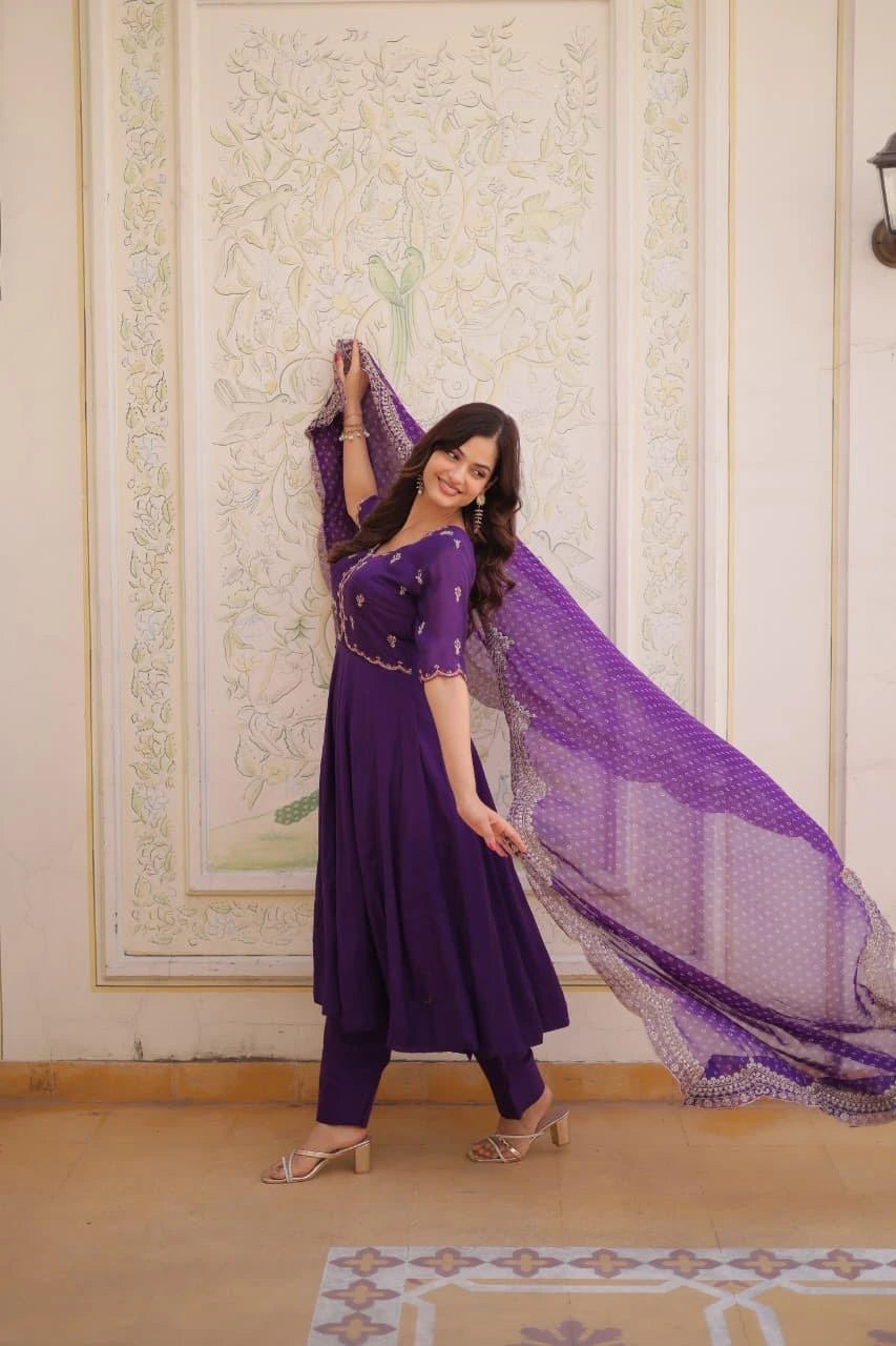 Woman in a purple traditional outfit with a matching dupatta against an ornate wall.