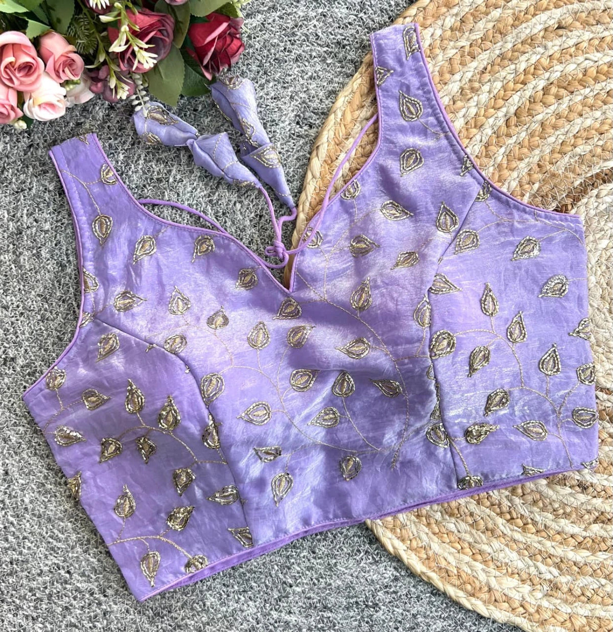Purple blouse with gold patterns on a textured surface with flowers.
