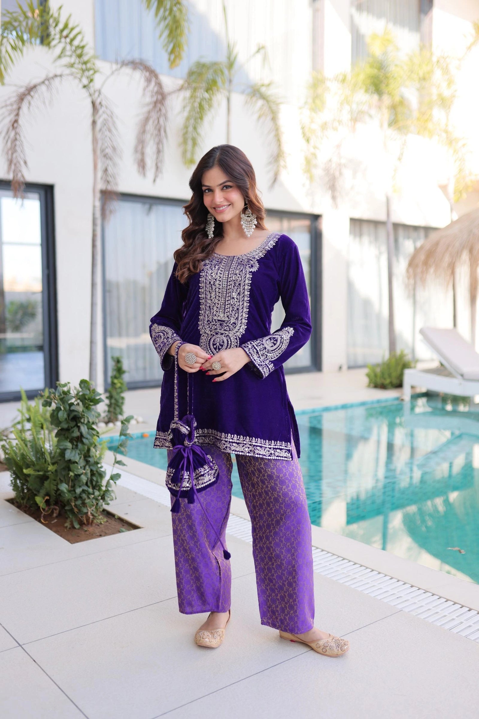 Woman in a purple traditional outfit standing by a pool with plants around.