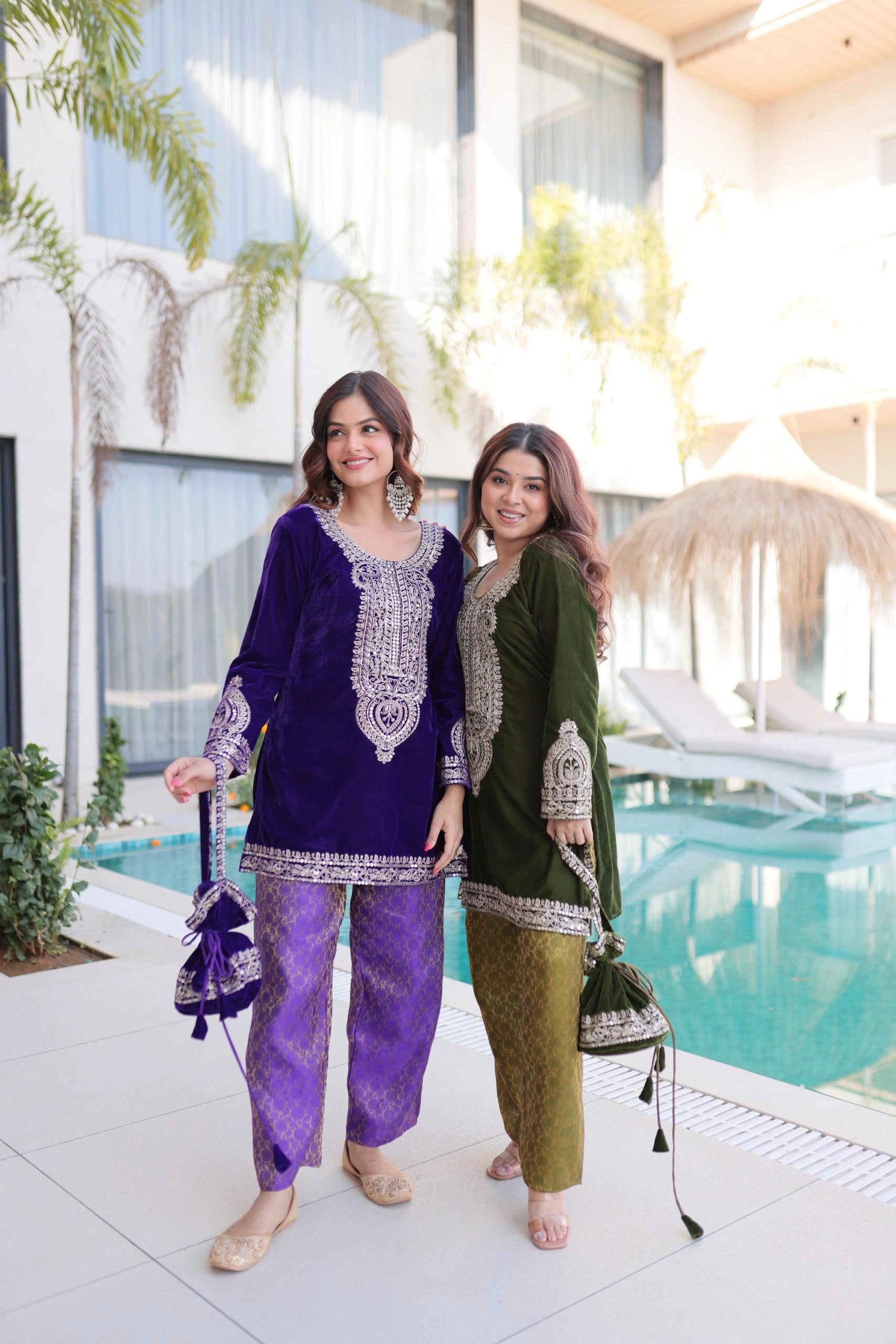 Two women in traditional outfits standing by a poolside.