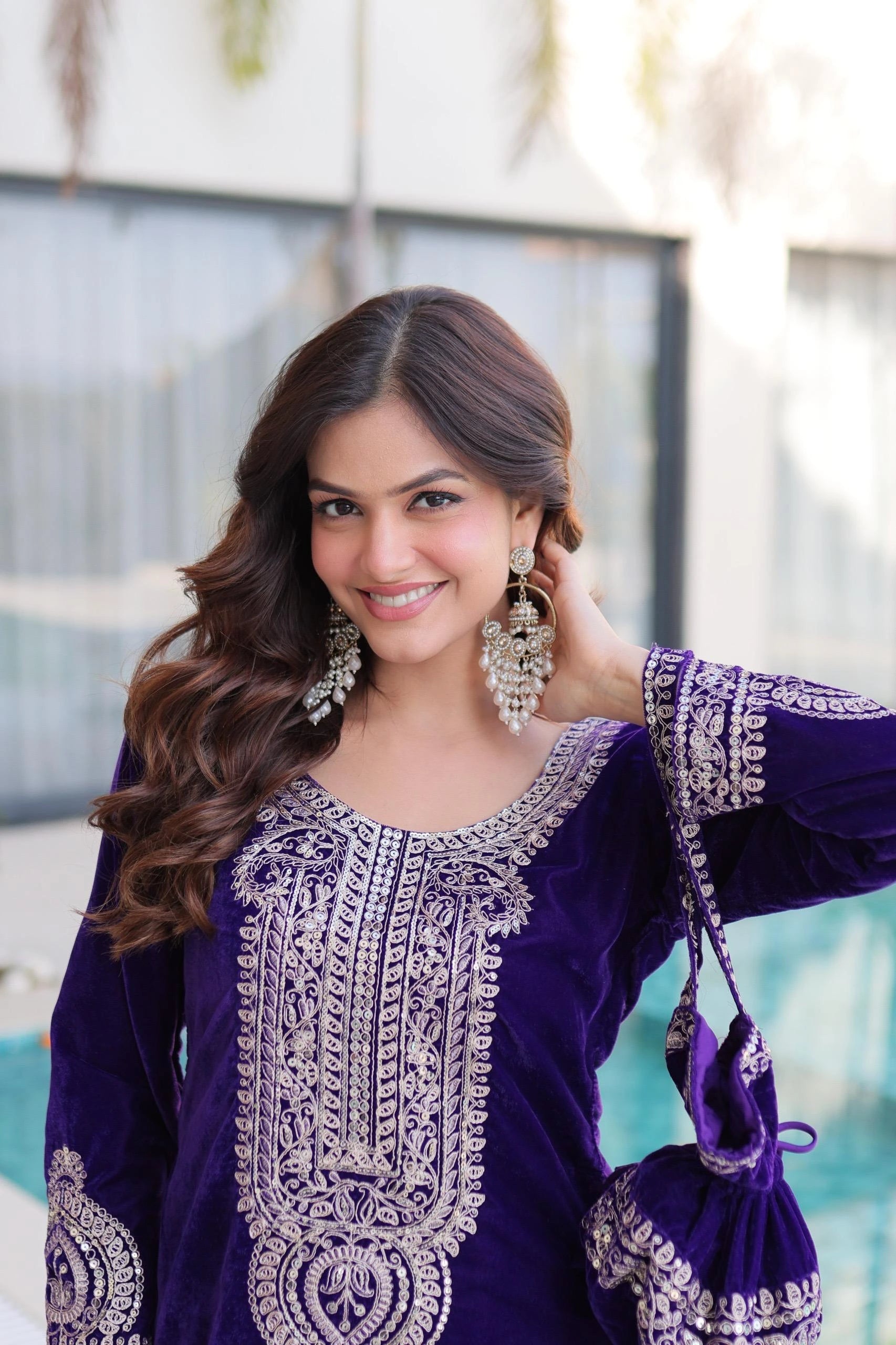 Woman in a purple traditional outfit with silver embroidery, holding a matching bag.