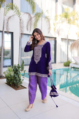 Woman in a purple outfit standing by a pool with plants and a building in the background