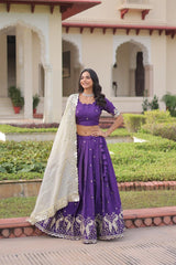 Woman in a purple traditional outfit standing in front of a building with greenery.
