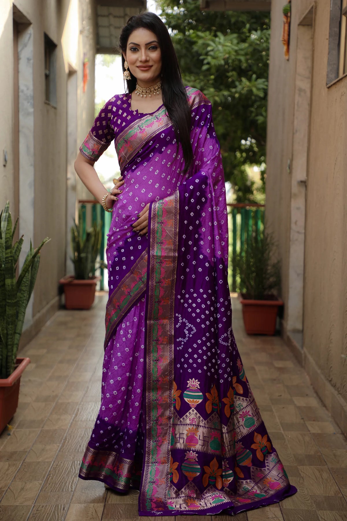 Woman wearing a purple saree with a patterned border in an outdoor setting.