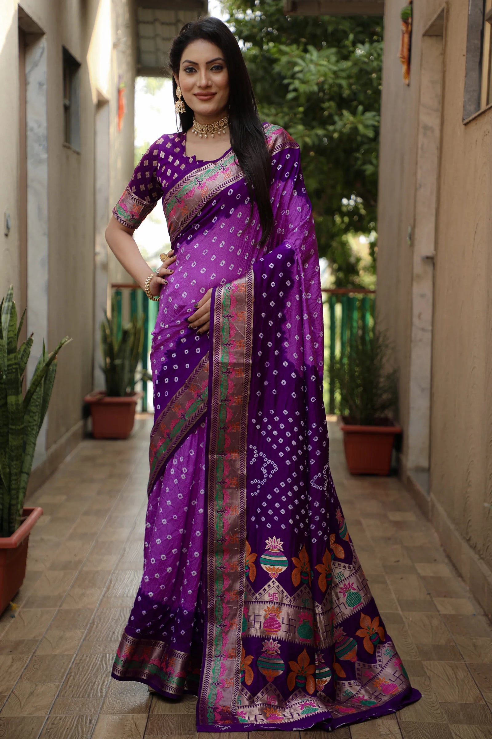 Woman wearing a purple saree with a patterned border in an outdoor setting.