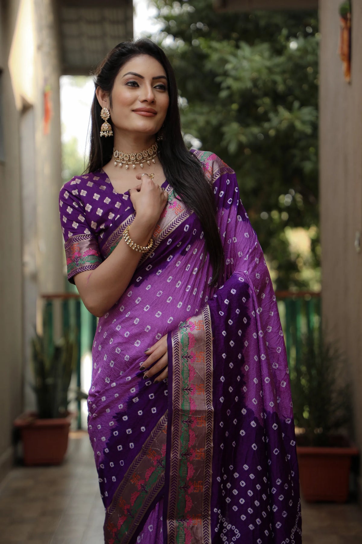 Woman wearing a purple saree with a pattern, standing outdoors.