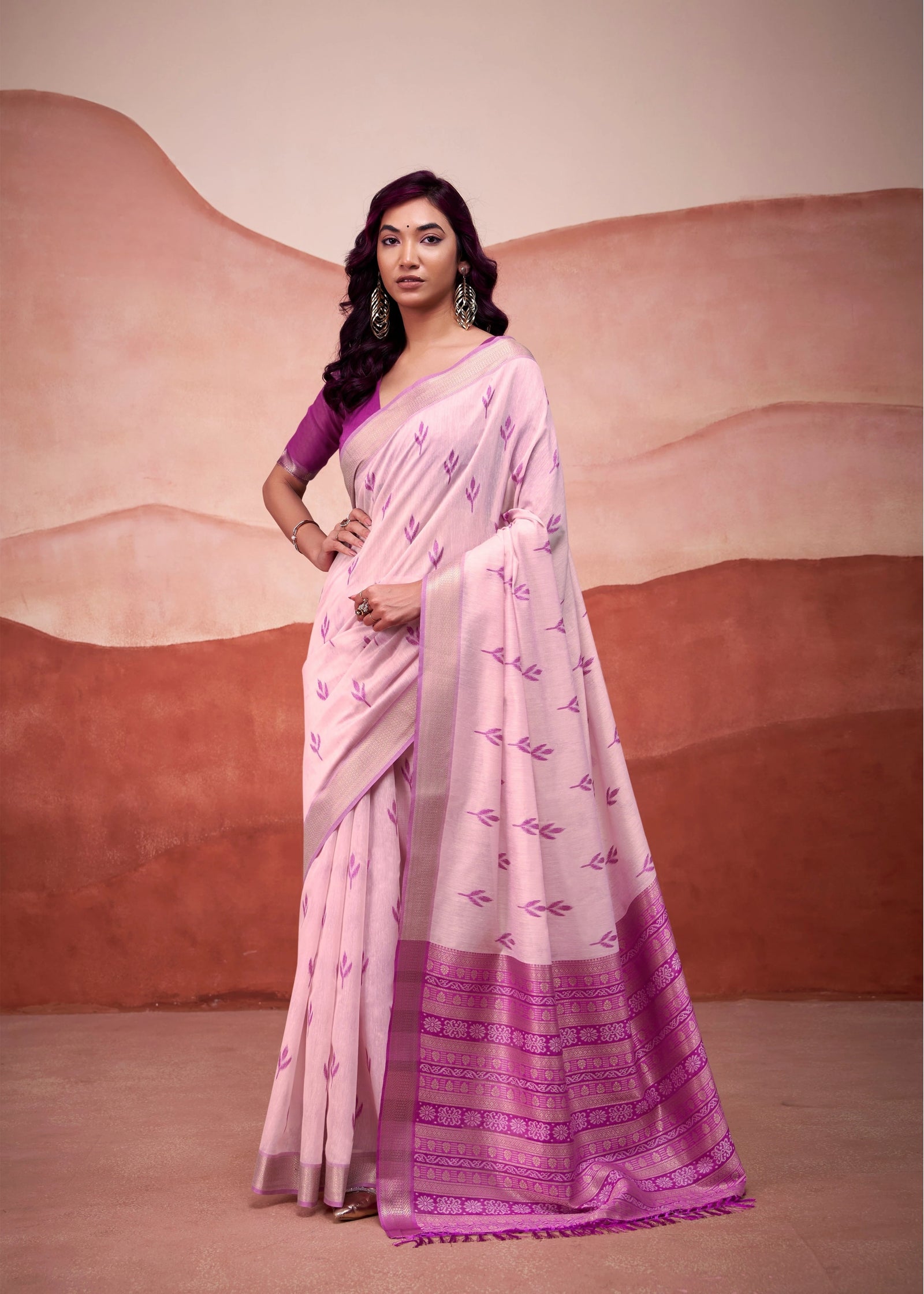Woman in a yellow and green saree standing in front of a stone wall.