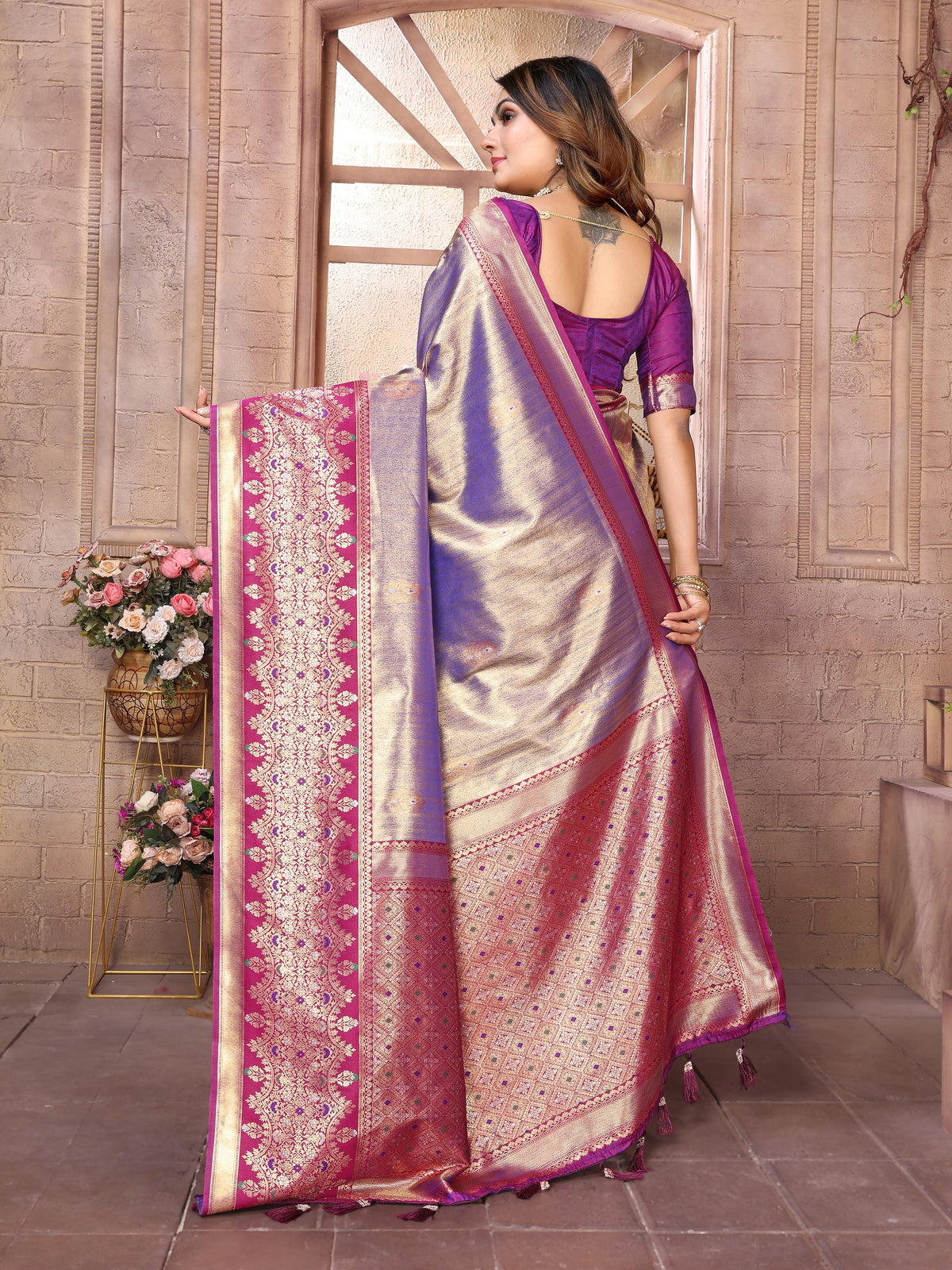 Woman holding a traditional saree with intricate patterns in a decorative setting.