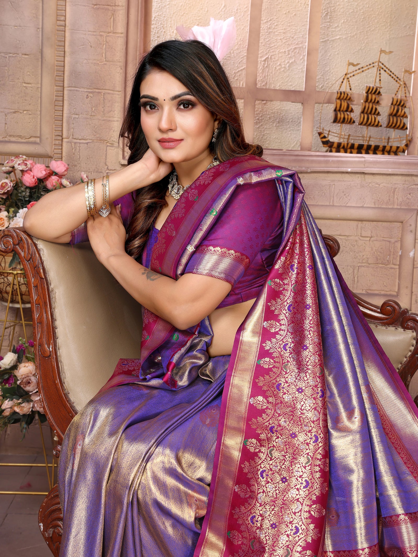 Woman in a purple saree sitting on a chair with decorative background