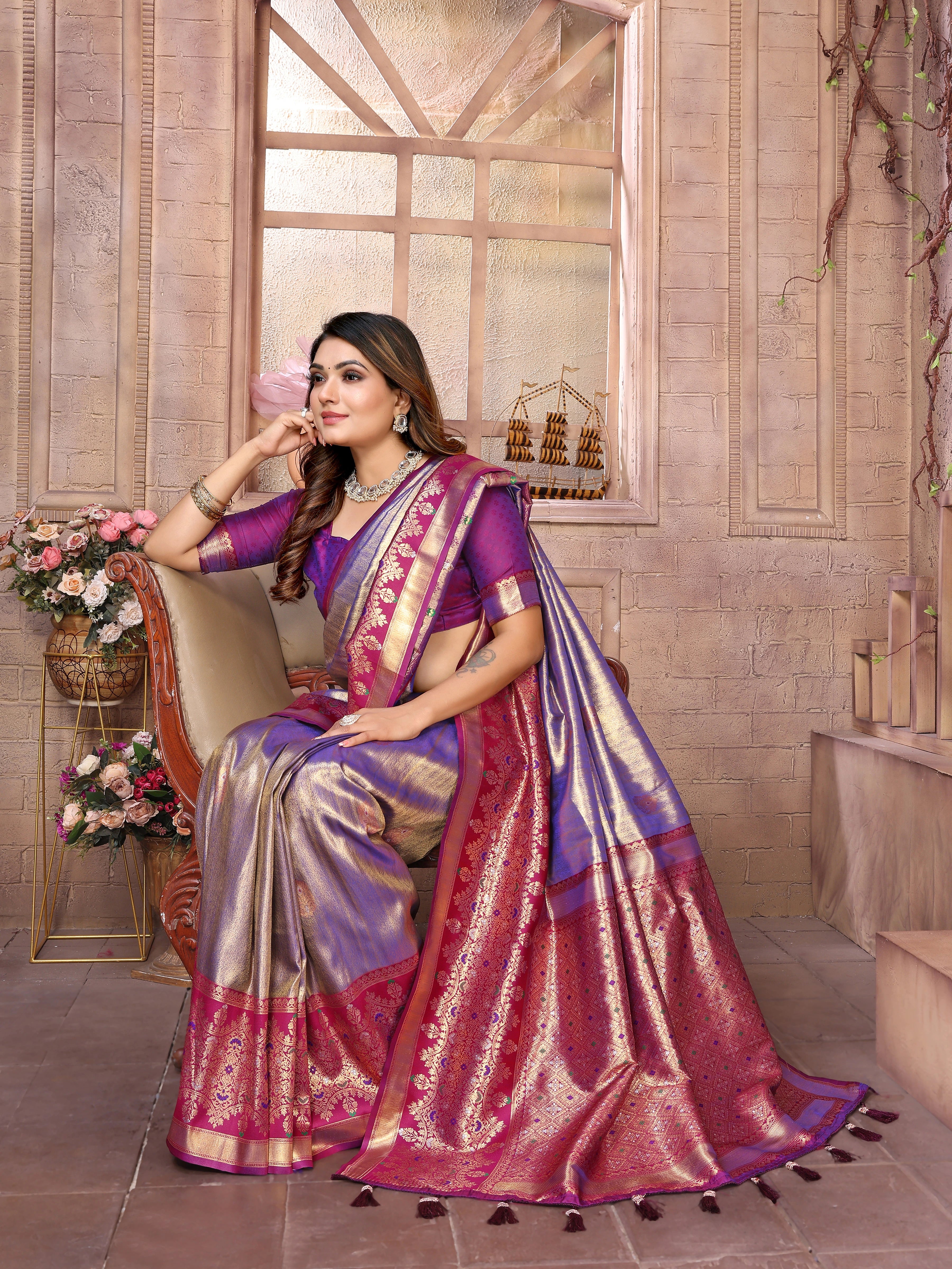Woman in a traditional saree sitting in a decorated room with flowers and decor.