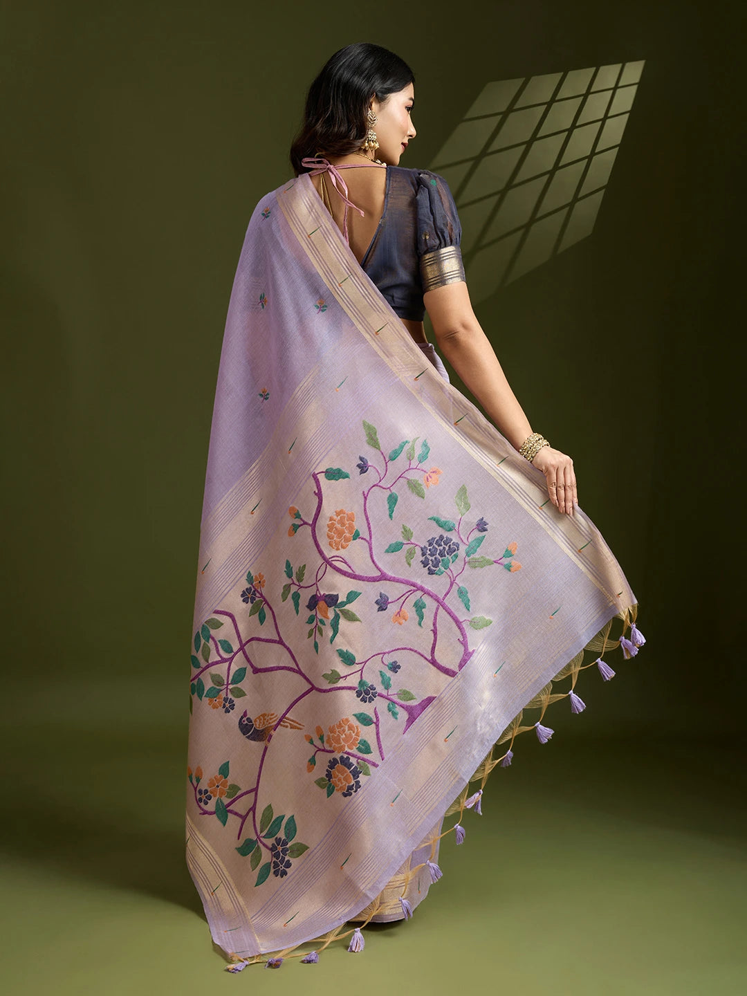 Woman wearing a light pink saree with floral embroidery and tassels on a green background
