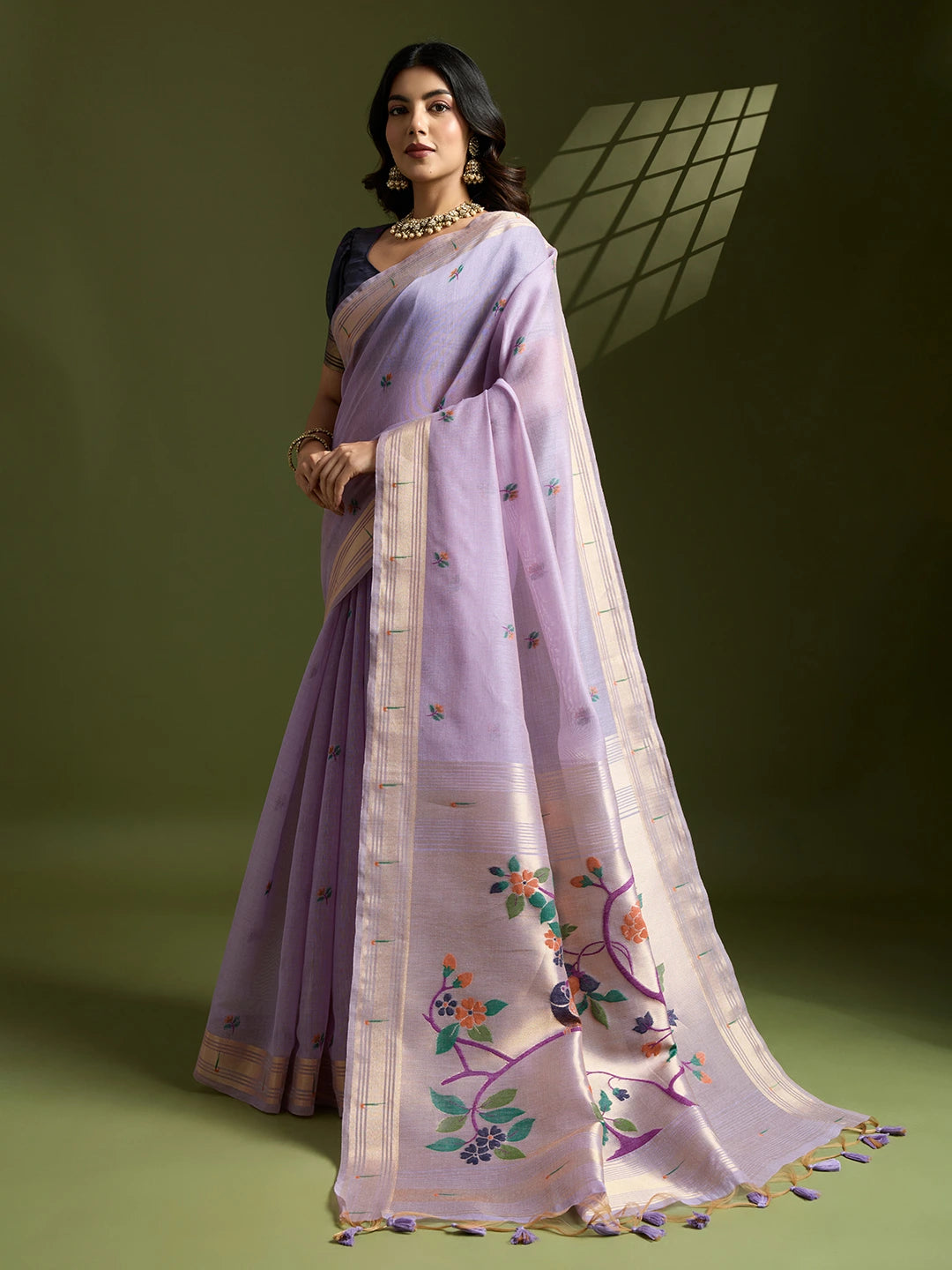 Woman wearing a light purple saree with floral embroidery on a green background