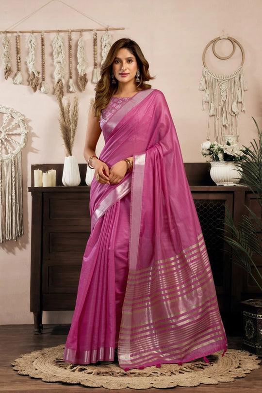 Woman in a pink saree standing in a room with decorative elements.