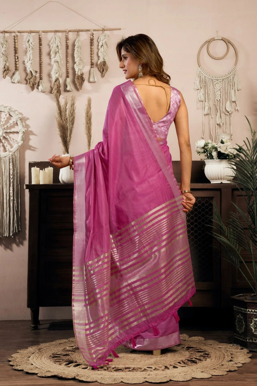 Woman in a pink saree standing in a room with decorative elements.