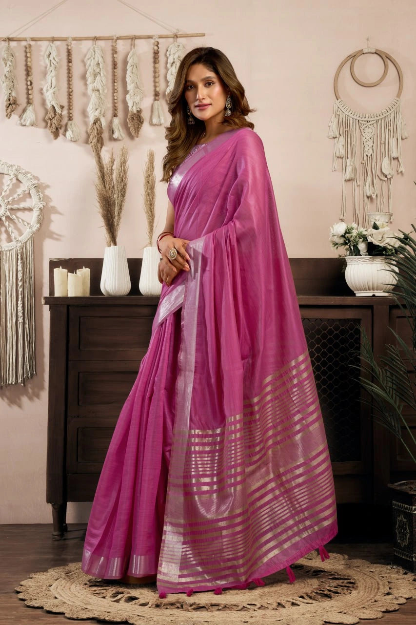 Woman in a pink saree standing in a room with decorative elements.