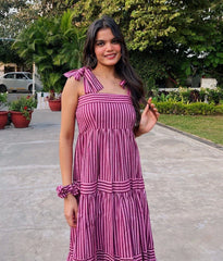 Woman in a pink and white striped dress standing outdoors with greenery in the background