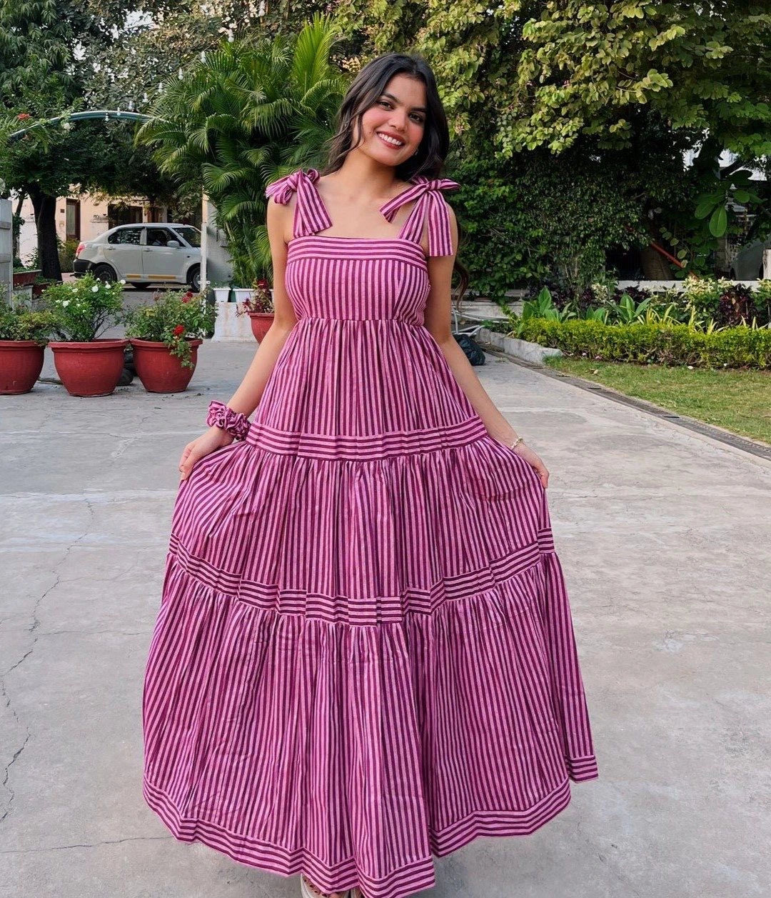 Woman in a pink and white striped dress standing outdoors with greenery in the background