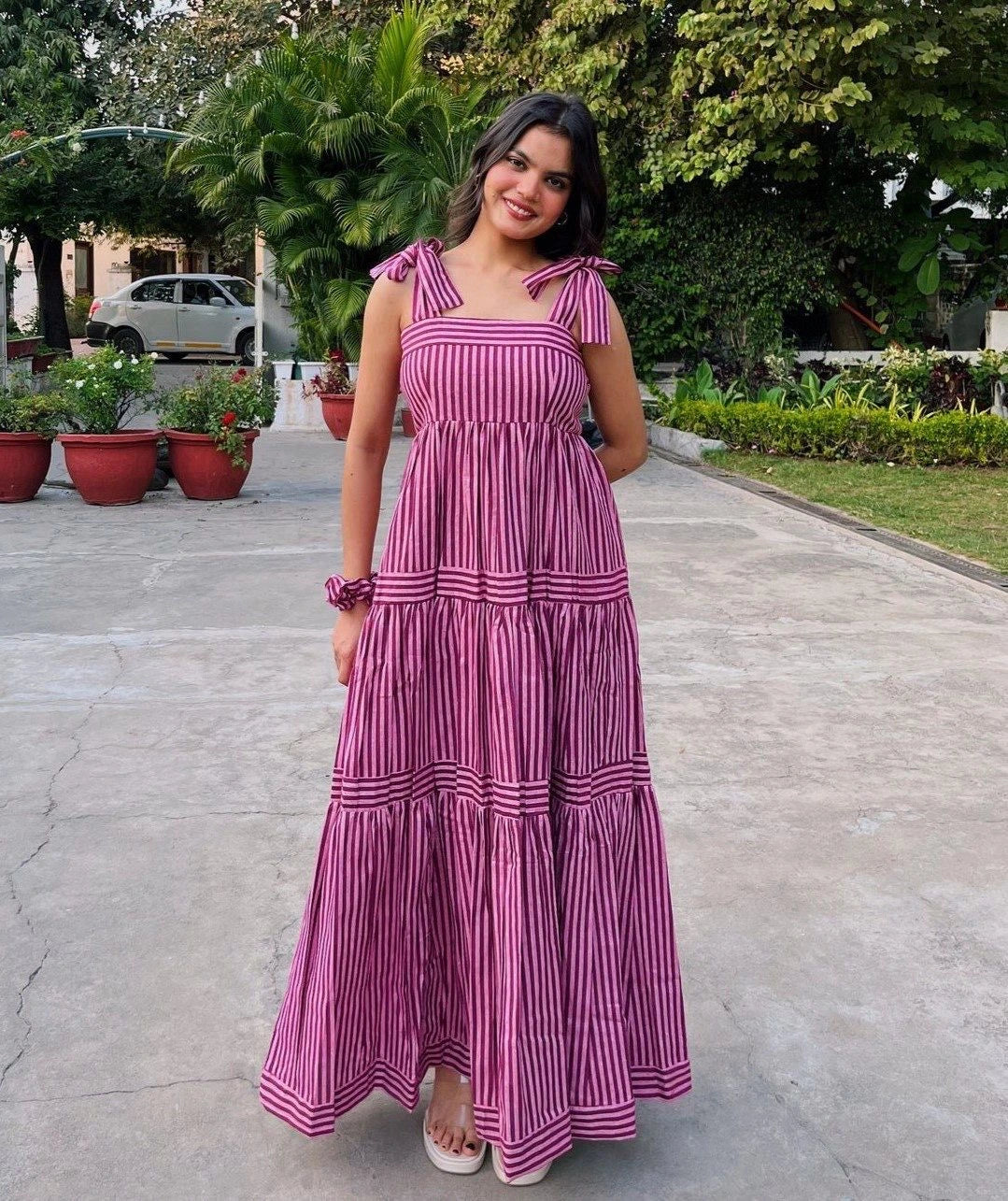 Woman in a pink and white striped dress standing on a paved path with greenery in the background