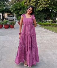 Woman in a pink and white striped dress standing on a paved path with greenery in the background