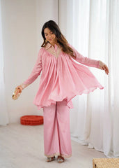 Woman wearing a pink traditional outfit in a bright room with white curtains.