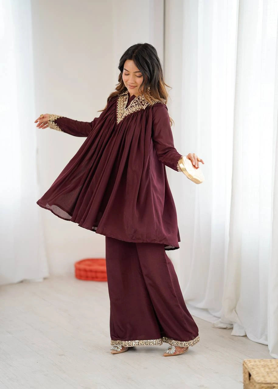 Woman wearing a burgundy traditional outfit with gold accents in a white room.