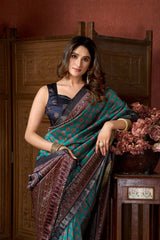 Woman in a traditional saree sitting in a room with wooden furniture and flowers.