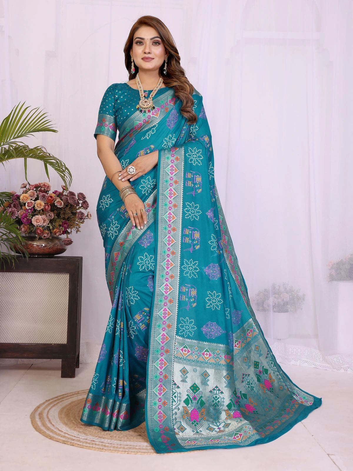 Woman wearing a teal saree with floral patterns indoors.
