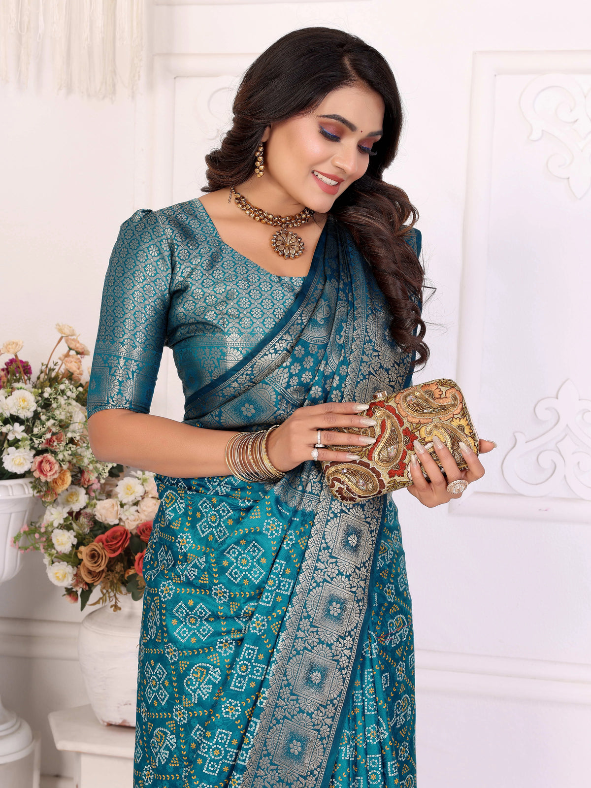 Woman in a blue saree holding a clutch against a white background