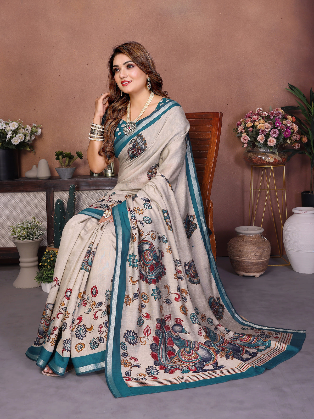 Woman in a saree with floral and peacock patterns in a decorated room.