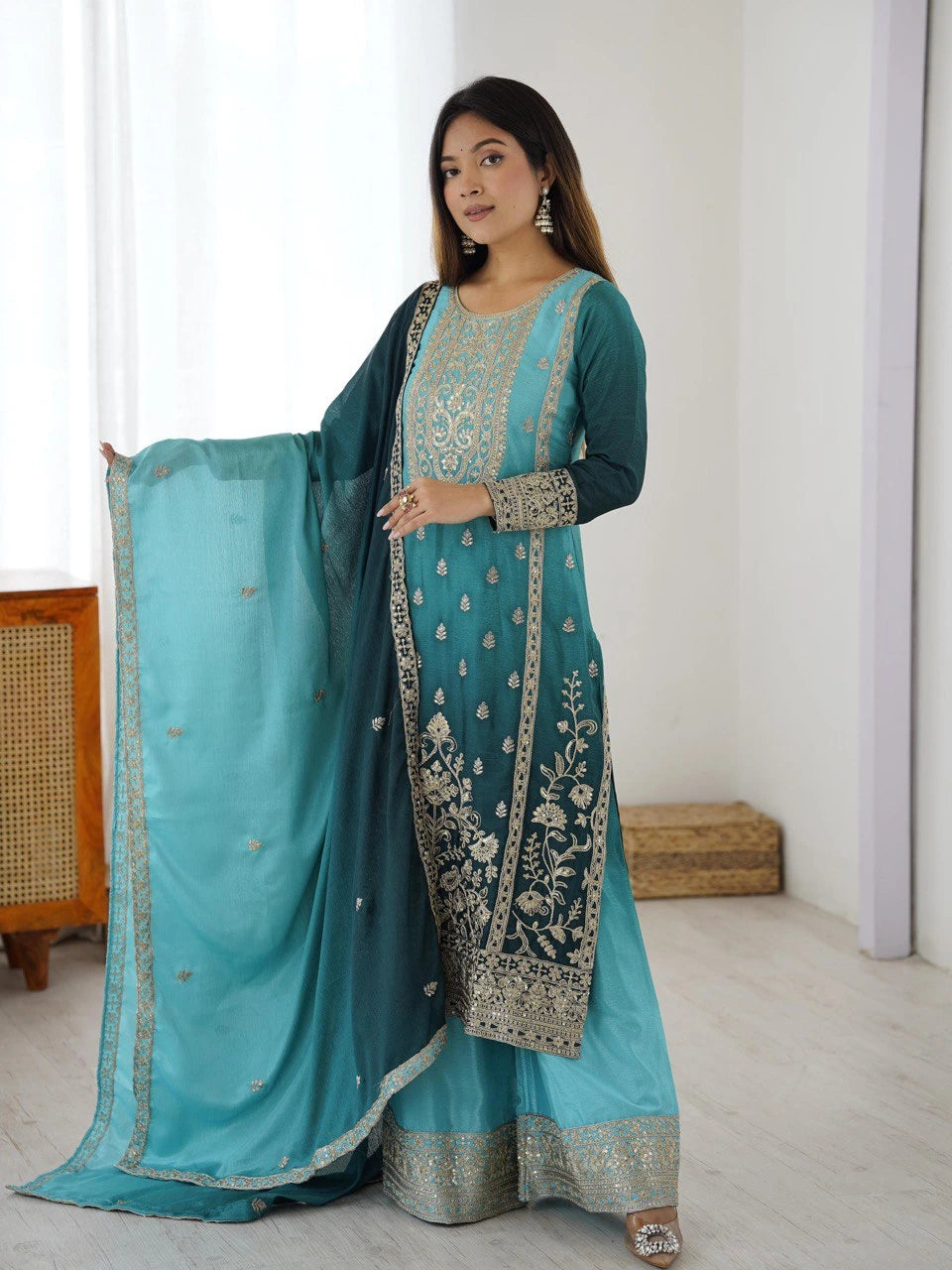 Woman wearing a traditional outfit with a turquoise dupatta and embroidered dress indoors.