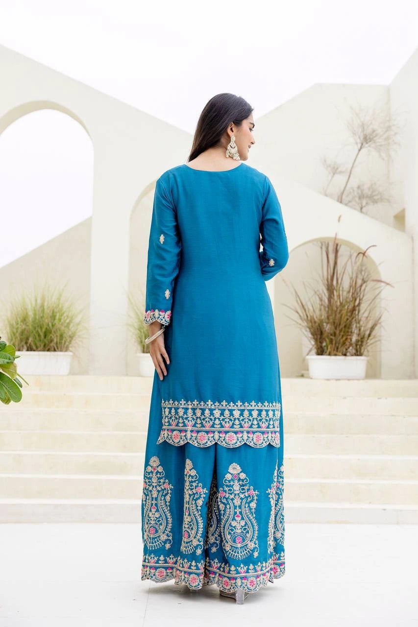 Woman wearing a blue traditional outfit with white patterns in an outdoor setting.