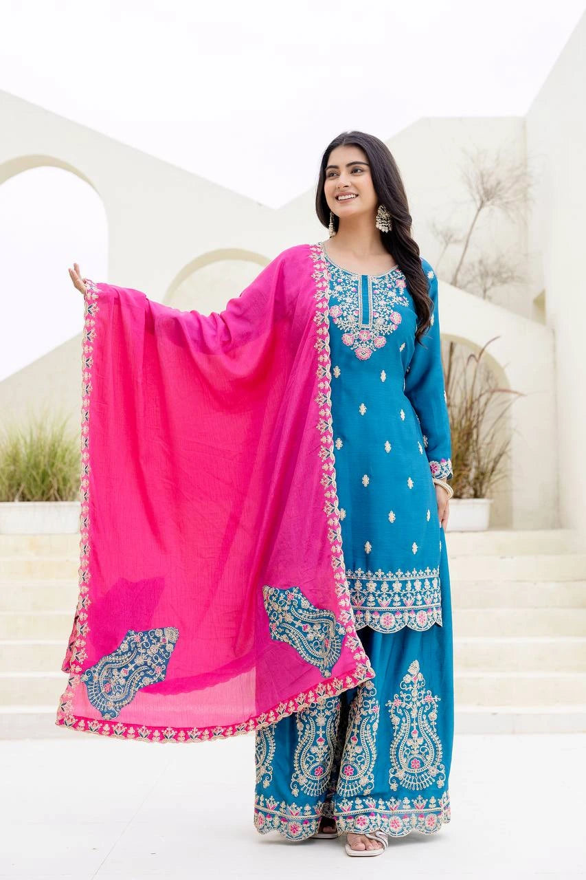 Woman in a blue and pink traditional outfit with embroidery, standing against a white background.