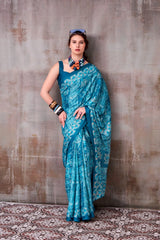 Woman wearing a blue saree with a pattern against a textured wall.