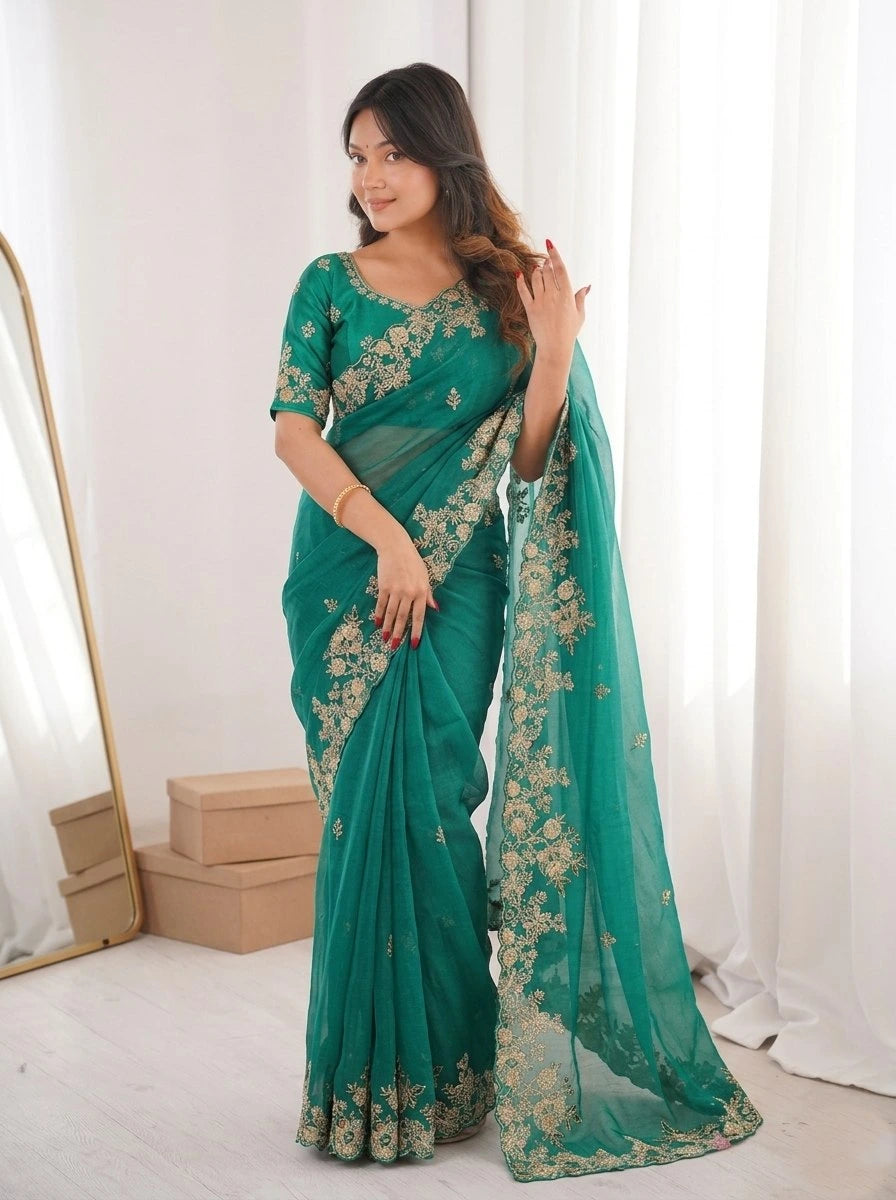Woman wearing a teal saree with gold embroidery in a bright room.
