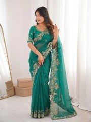 Woman wearing a teal saree with gold embroidery in a bright room.
