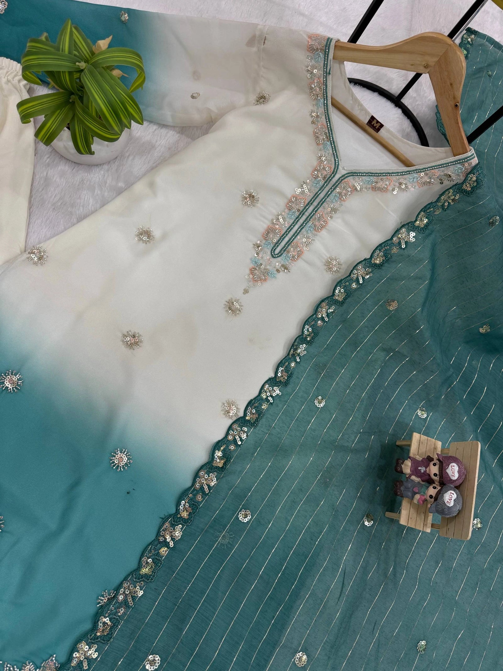 Teal and white embroidered garment on a hanger with a small table and chairs model below.